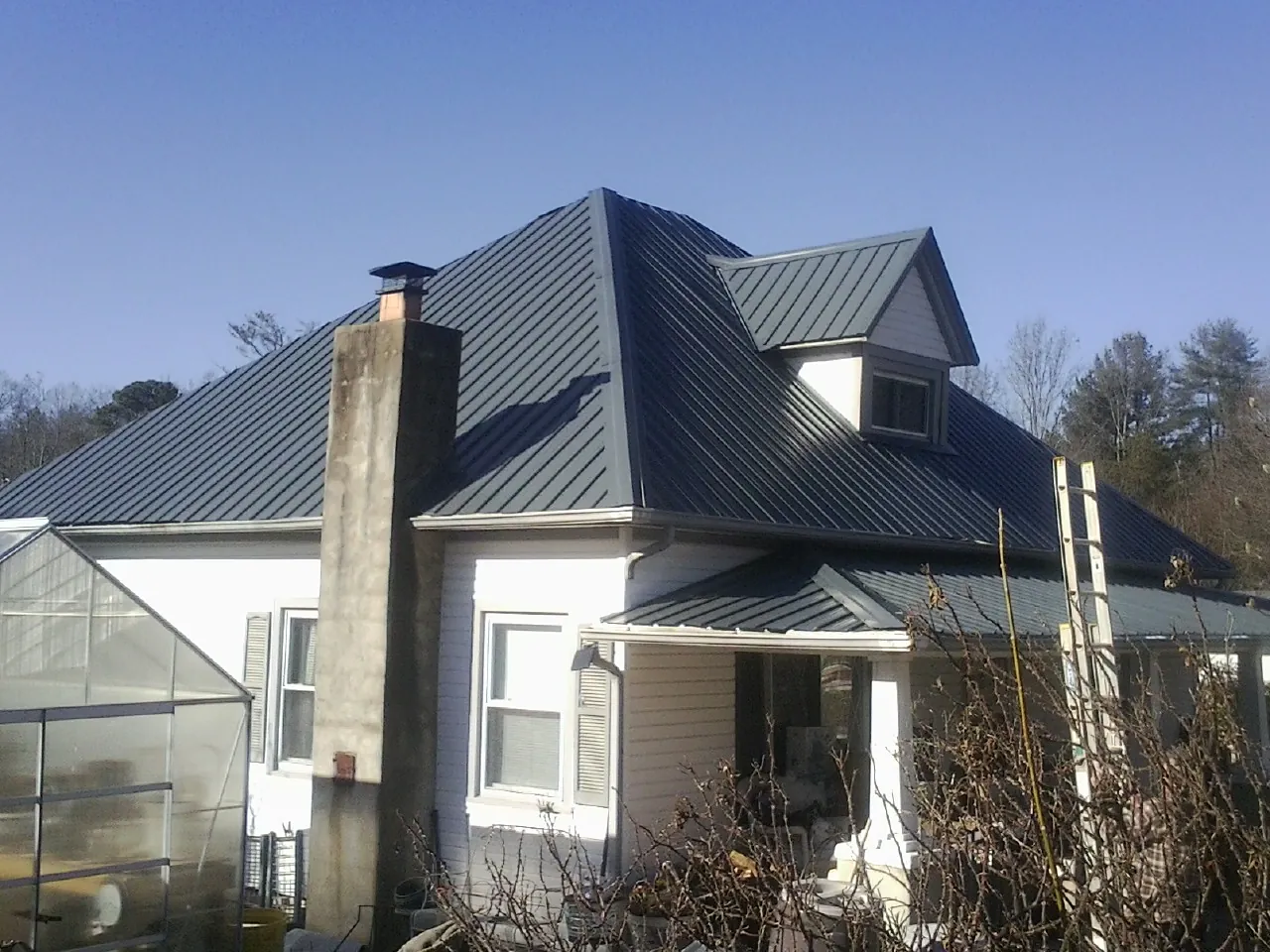 Dark blue standing seam metal roof on a white farmhouse with dormer — Slate & Tile Roof Repair by Roofing Brothers in Arlington